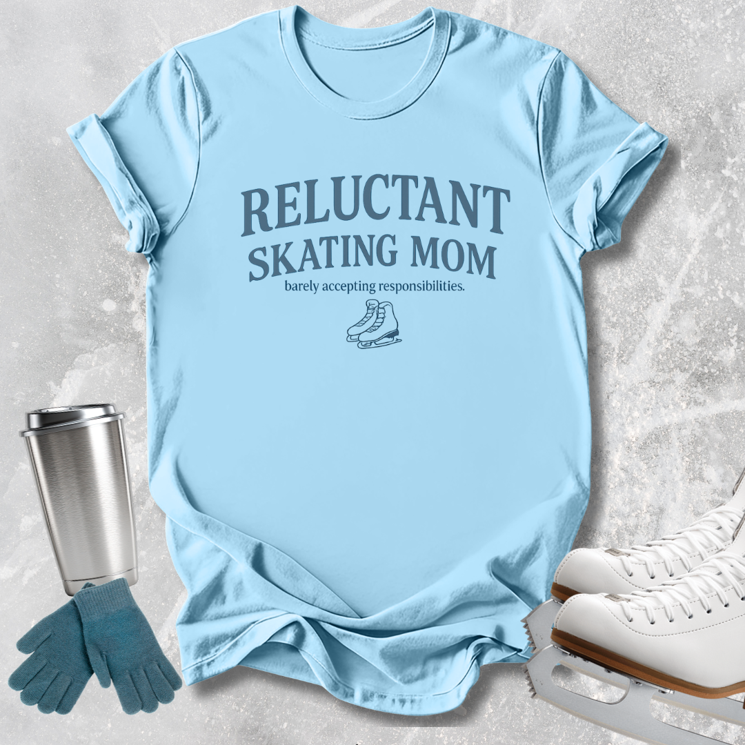 A light blue graphic t-shirt laid flat on a textured gray background, featuring the text 'RELUCTANT SKATING MOM' and 'barely accepting responsibilities.' with a small ice skate illustration.