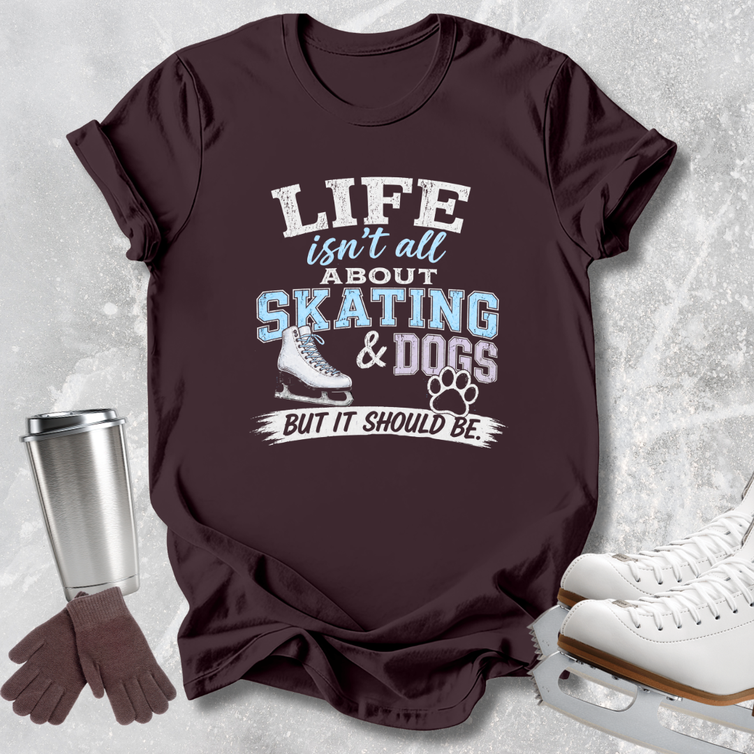 A dark brown graphic t-shirt laid flat on a light gray textured background, styled with ice skates, gloves, and a metal tumbler. The shirt features the text 'LIFE isn't all ABOUT SKATING & DOGS BUT IT SHOULD BE.