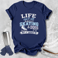 A navy blue graphic t-shirt laid flat on a light gray textured background, featuring the text 'LIFE isn't all ABOUT SKATING & DOGS BUT IT SHOULD BE.' in white and light blue, alongside a skate boot graphic and paw print.