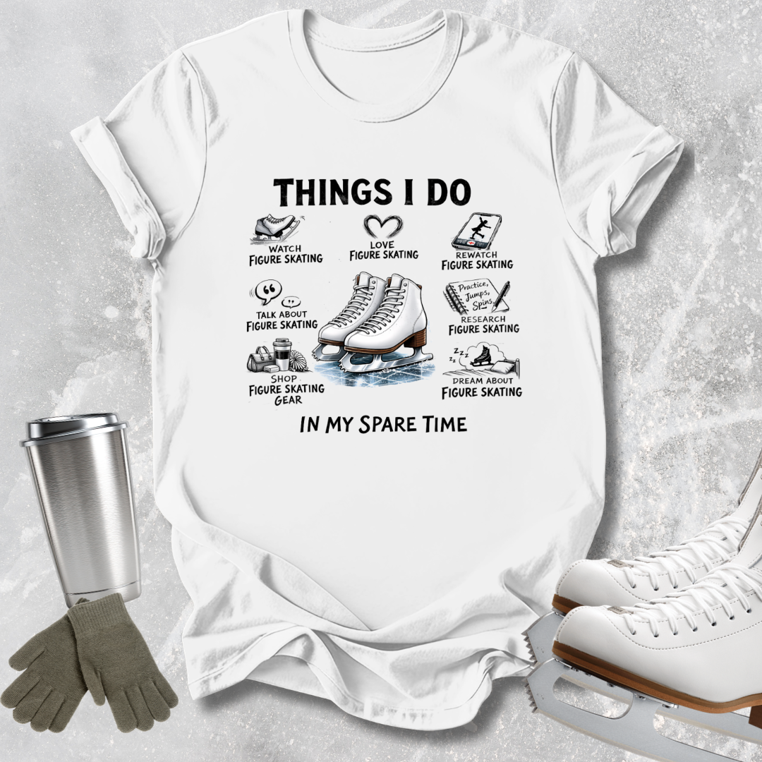 A white graphic t-shirt laid flat on a light gray textured surface, featuring black text and illustrations related to figure skating. Surrounding props include a metal travel mug, gray gloves, and white ice skates.