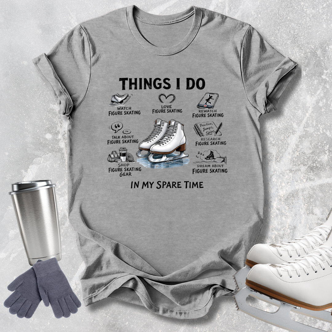 A heather gray graphic t-shirt featuring a figure skating themed print with illustrations and text, styled in a flat-lay arrangement with ice skates, gloves, and a travel tumbler on a textured light gray background.