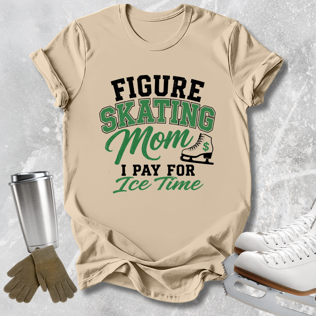 A beige graphic T-shirt laid flat on a light gray textured surface, with ice skates, gloves, and a travel tumbler as props. The shirt reads “FIGURE SKATING Mom I PAY FOR Ice Time” in black and green lettering with a small ice skate illustration.
