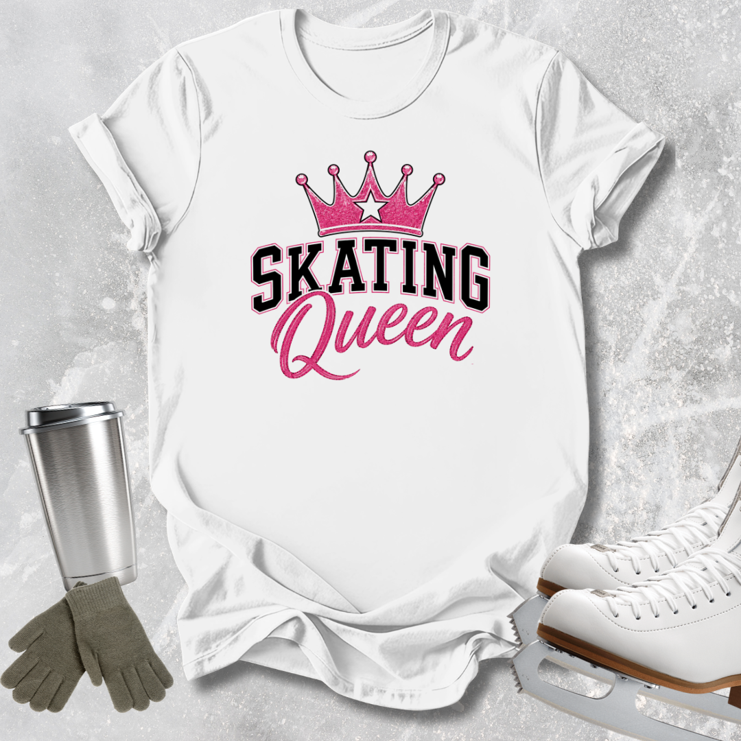 A white short-sleeve T-shirt laid flat on a light gray textured surface, featuring a pink crown graphic above the words 'SKATING Queen' in black and pink lettering. Ice skates, gloves, and a metal cup are arranged around the shirt as styling props.