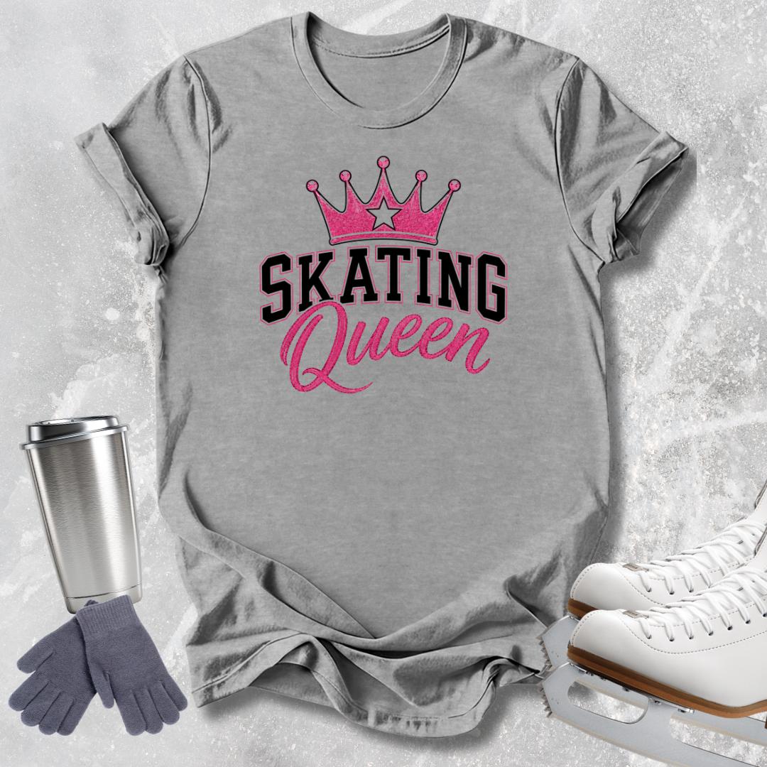 A heather gray graphic T-shirt laid flat on a light textured background, featuring a pink crown above the words 'SKATING Queen' in black and pink script. A stainless steel travel mug, gray gloves, and white ice skates are arranged around the shirt as styled props.