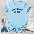 A light blue short-sleeve T-shirt with the words 'SOMEWHERE ON ICE' printed in black across the chest, styled in a flat lay with ice skates, gloves, and a metal cup on a light gray textured background.
