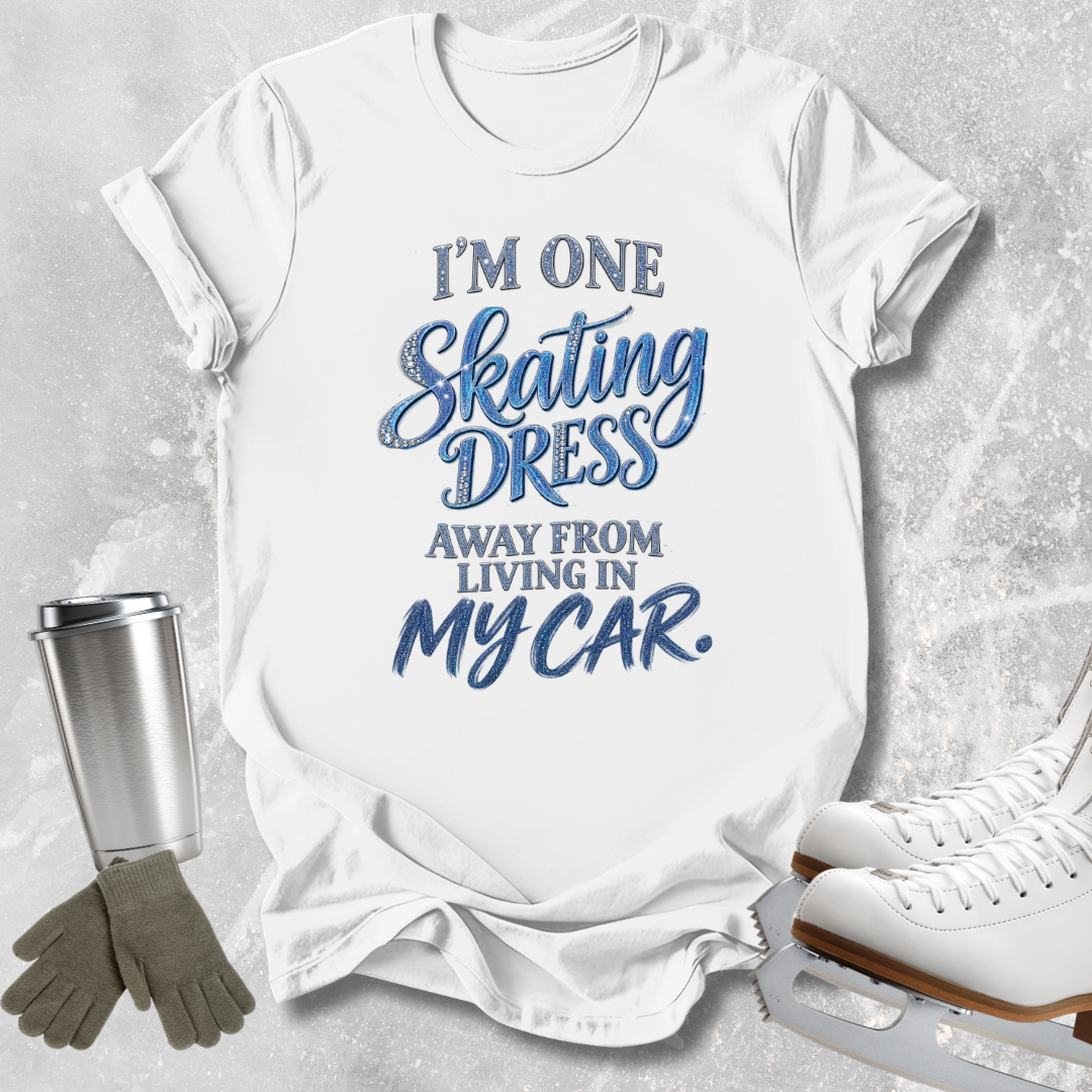 A white graphic t-shirt with blue text reading 'I'M ONE Skating DRESS AWAY FROM LIVING IN MY CAR.' displayed in a flat-lay arrangement with ice skates, gloves, and a travel tumbler on a light gray textured background.