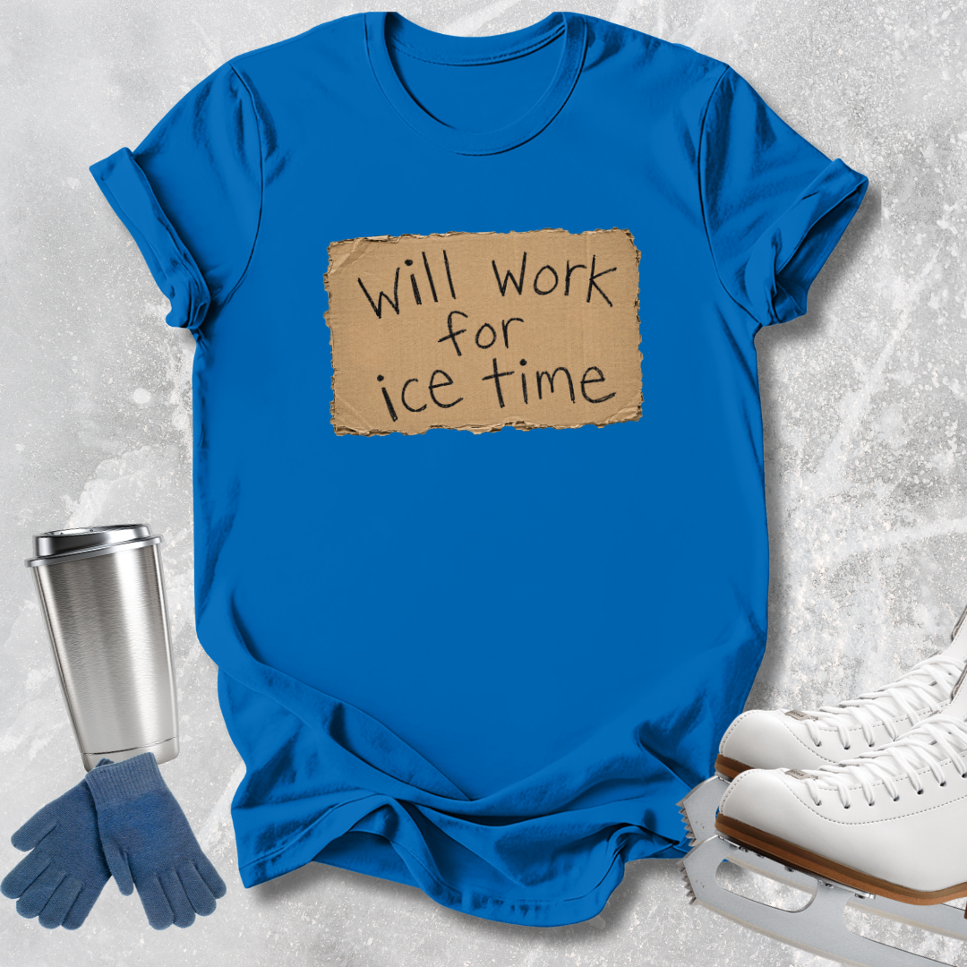 A bright blue short-sleeve T-shirt laid flat on a light gray textured surface, featuring a tan cardboard-style graphic with the handwritten text 'Will work for ice time.' Blue gloves, a silver travel tumbler, and white ice skates are arranged around the shirt as styling props.