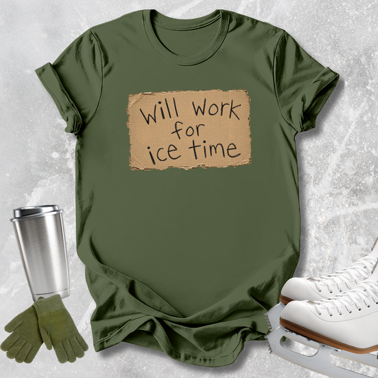An olive green graphic t-shirt with a cardboard sign design that reads 'Will work for ice time' in black handwritten text. The t-shirt is styled in a flat-lay arrangement on a light gray textured background, accompanied by white ice skates, green gloves, and a silver travel mug.