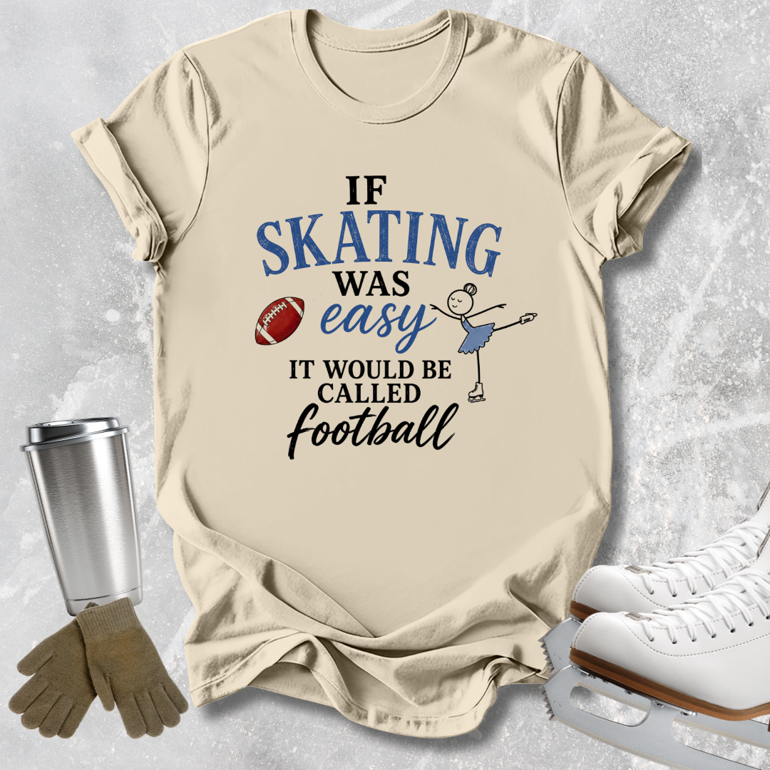 A beige graphic t-shirt laid flat on a light gray textured background, styled with ice skates, gloves, and a metal cup. The shirt features a printed design that reads 'IF SKATING WAS easy IT WOULD BE CALLED football' in blue and black lettering, accompanied by a small stick-figure skater and a football graphic.