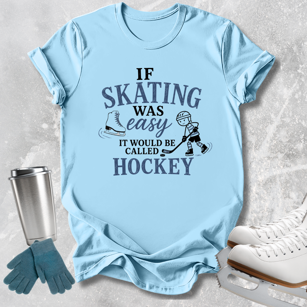 A light blue graphic t-shirt laid flat on a textured gray background, featuring a dark blue print that reads 'IF SKATING WAS easy IT WOULD BE CALLED HOCKEY' with skater illustrations. Ice skates, gloves, and a metal tumbler are styled around the shirt.