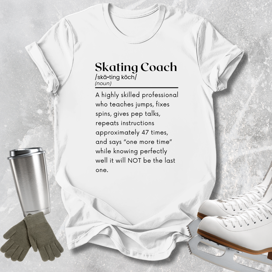A white graphic T-shirt laid flat on a light gray textured surface, printed with a black dictionary-style definition reading 'Skating Coach.' Surrounding props include a metal travel tumbler, gray gloves, and white ice skates.