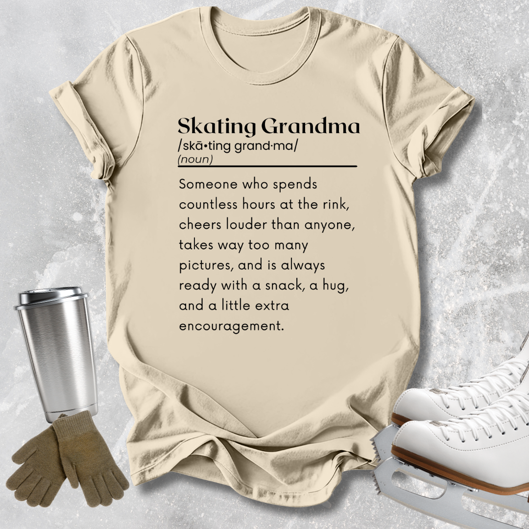 A beige graphic T-shirt laid flat on a light gray textured surface, with skating-themed props including white ice skates, gloves, and a metal cup. The shirt reads 'Skating Grandma' with a dictionary-style definition printed in black text.