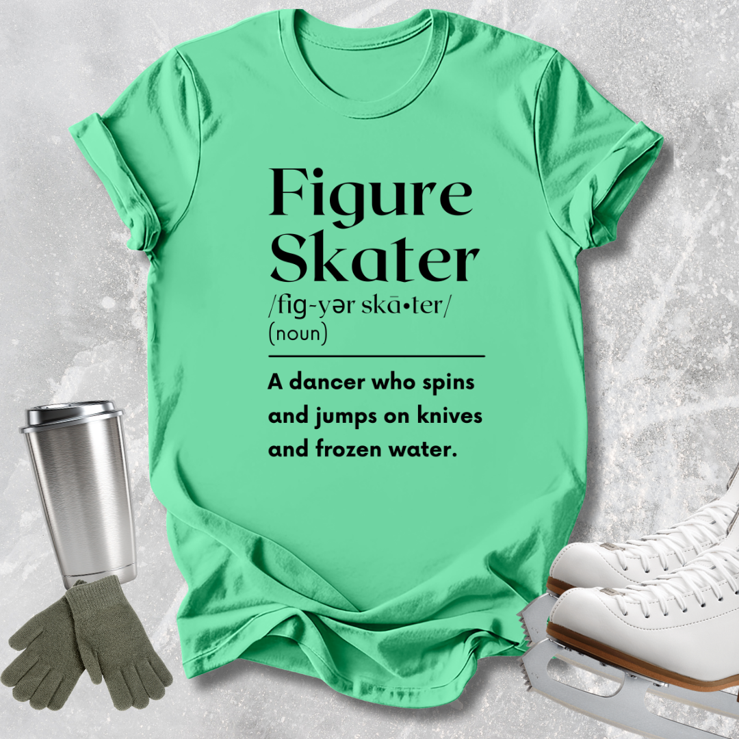 A mint green graphic t-shirt laid flat on a light gray textured background, styled with ice skates, gloves, and a metal tumbler. The t-shirt features a black printed definition of 'Figure Skater' with a humorous description.
