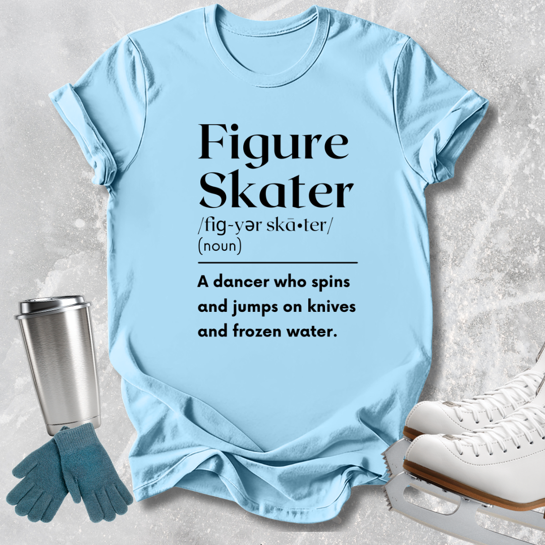 A light blue graphic T-shirt laid flat on a textured gray surface, with black printed text defining 'Figure Skater.' Surrounding props include a metal travel tumbler, teal gloves, and white ice skates.