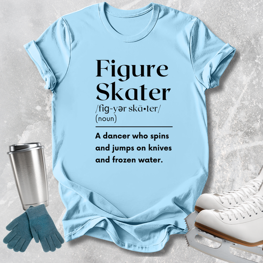 A light blue graphic T-shirt laid flat on a textured gray surface, with black printed text defining 'Figure Skater.' Surrounding props include a metal travel tumbler, teal gloves, and white ice skates.