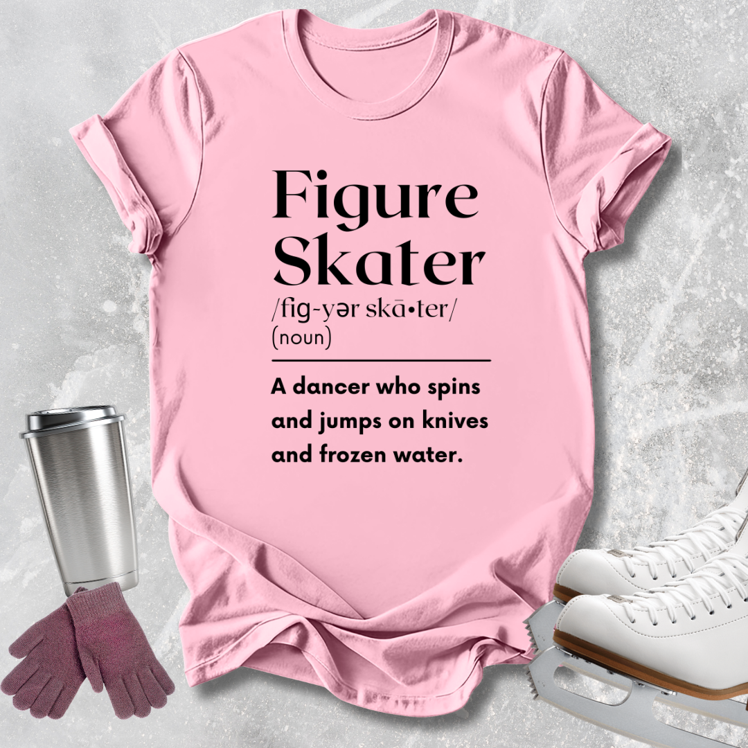 A pink short-sleeve graphic T-shirt laid flat on a light gray textured surface, with black text reading 'Figure Skater' and a definition-style phrase below. Ice skates, gloves, and a metal tumbler are styled around the shirt as props.