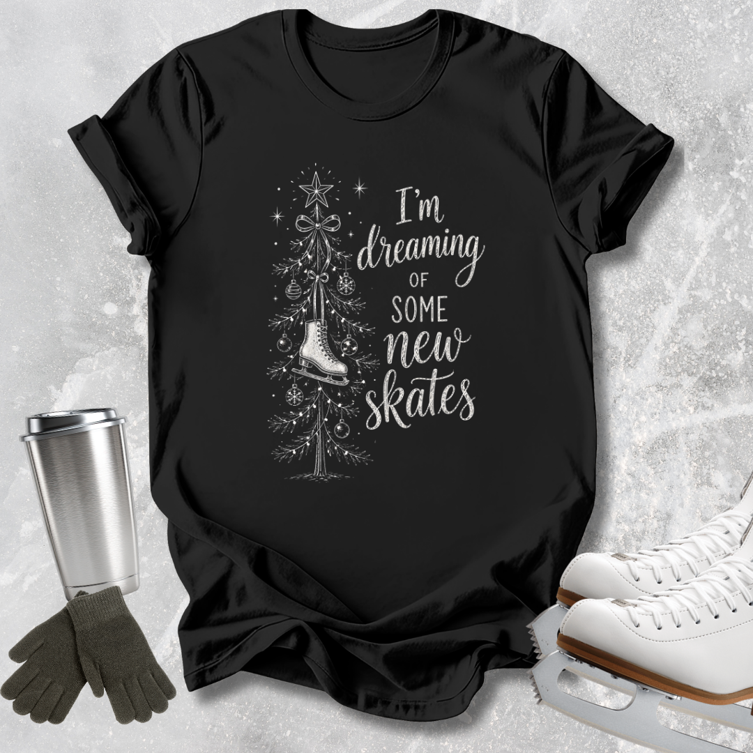 A black short-sleeve T-shirt laid flat on a light gray textured surface, printed with the phrase 'HAPPIEST ON ICE' in light blue. Ice skate boots, gloves, and a metal cup are arranged around the shirt as styled props.