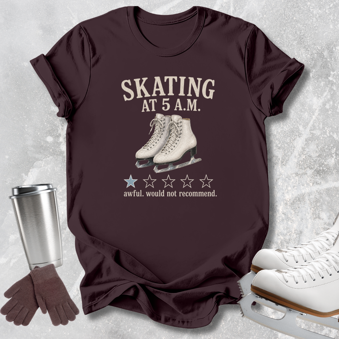 A dark maroon short-sleeve graphic T-shirt laid flat on a light gray textured surface, with a printed design reading 'SKATING AT 5 A.M.