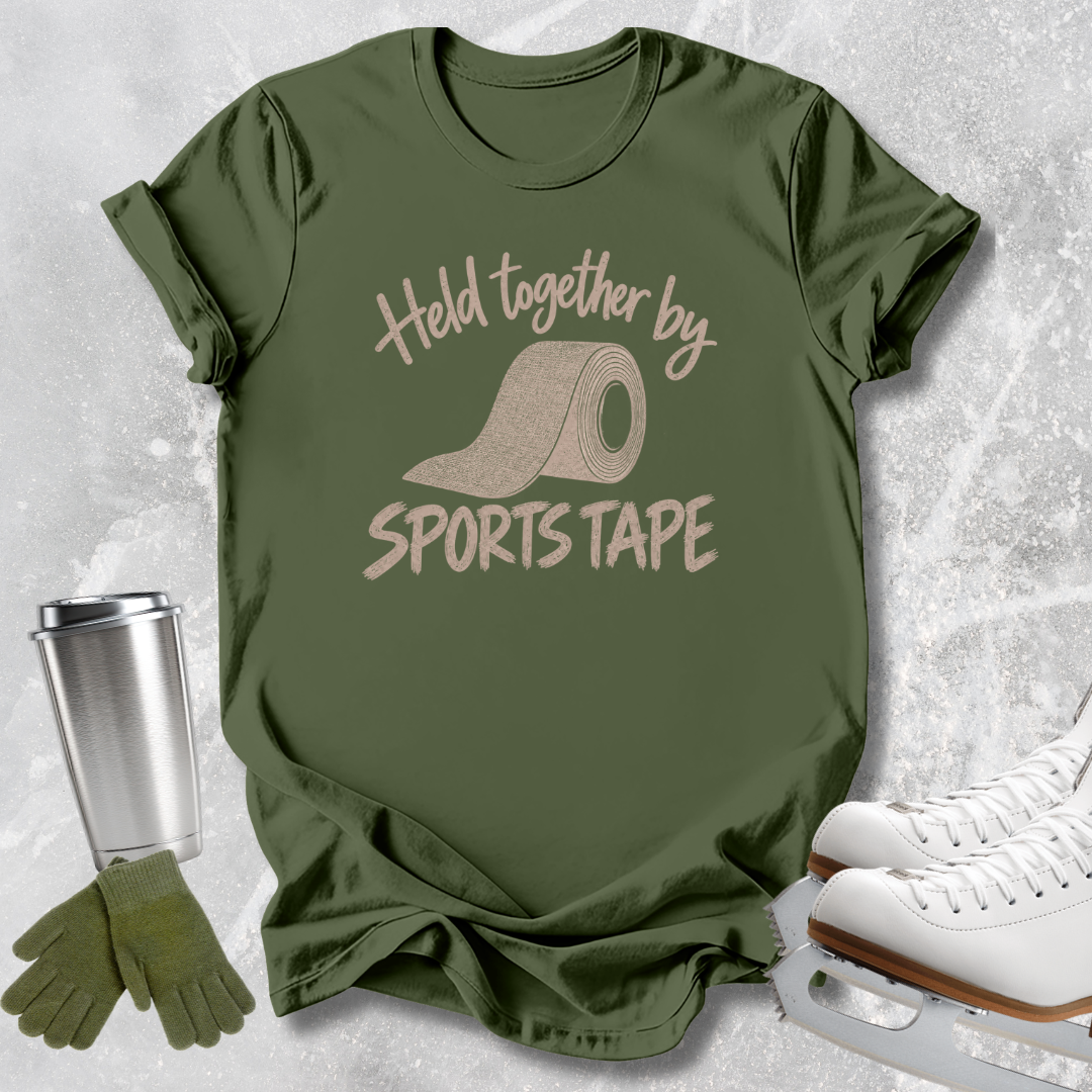 An olive green graphic t-shirt featuring the text 'Held together by SPORTS TAPE' with a roll of sports tape illustration, styled in a flat lay with ice skates, a travel tumbler, and gloves on a light gray textured background.