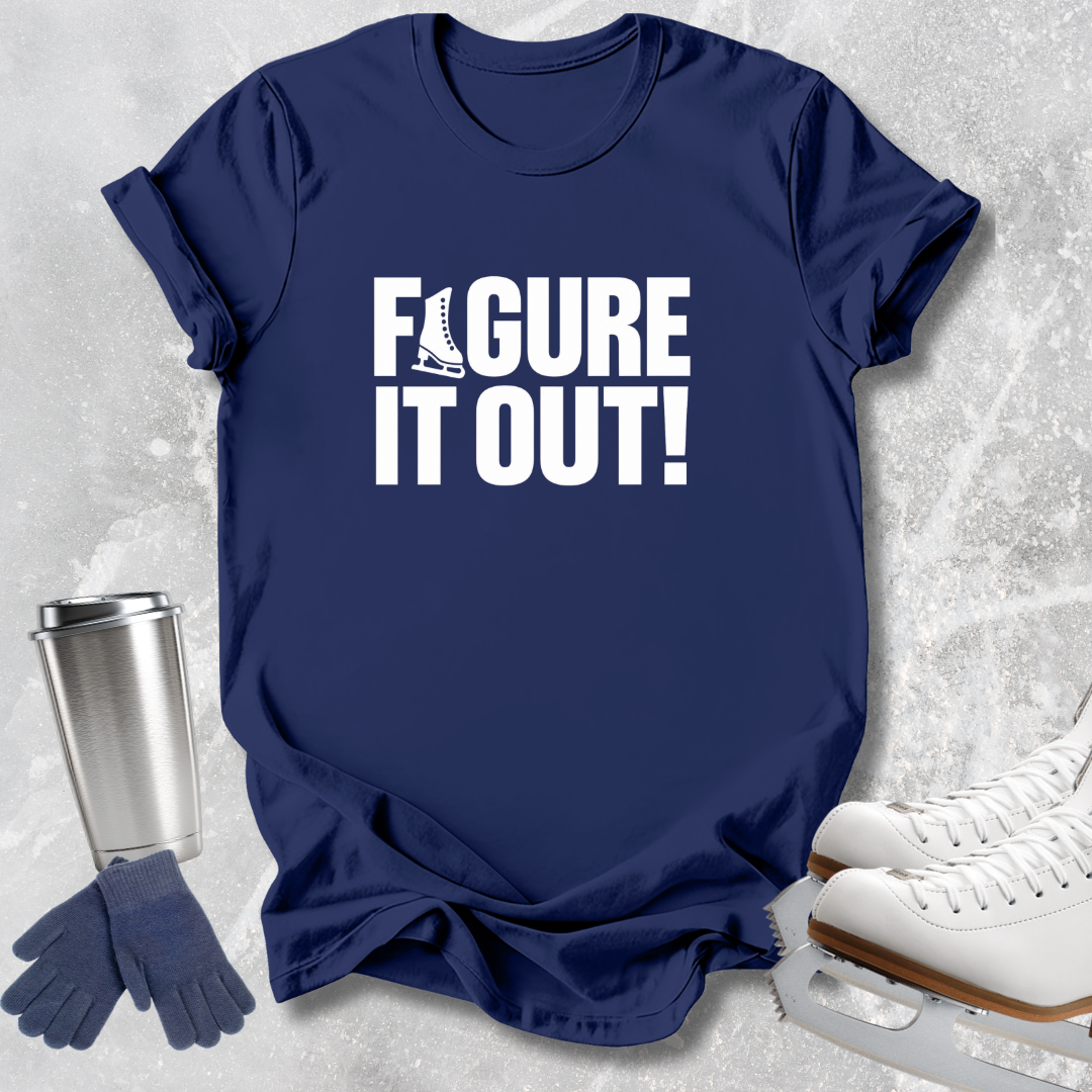 A navy blue graphic t-shirt with the white text 'FIGURE IT OUT!' and a small ice skate illustration, styled in a flat lay with ice skates, gloves, and a metal tumbler on a light gray textured background.
