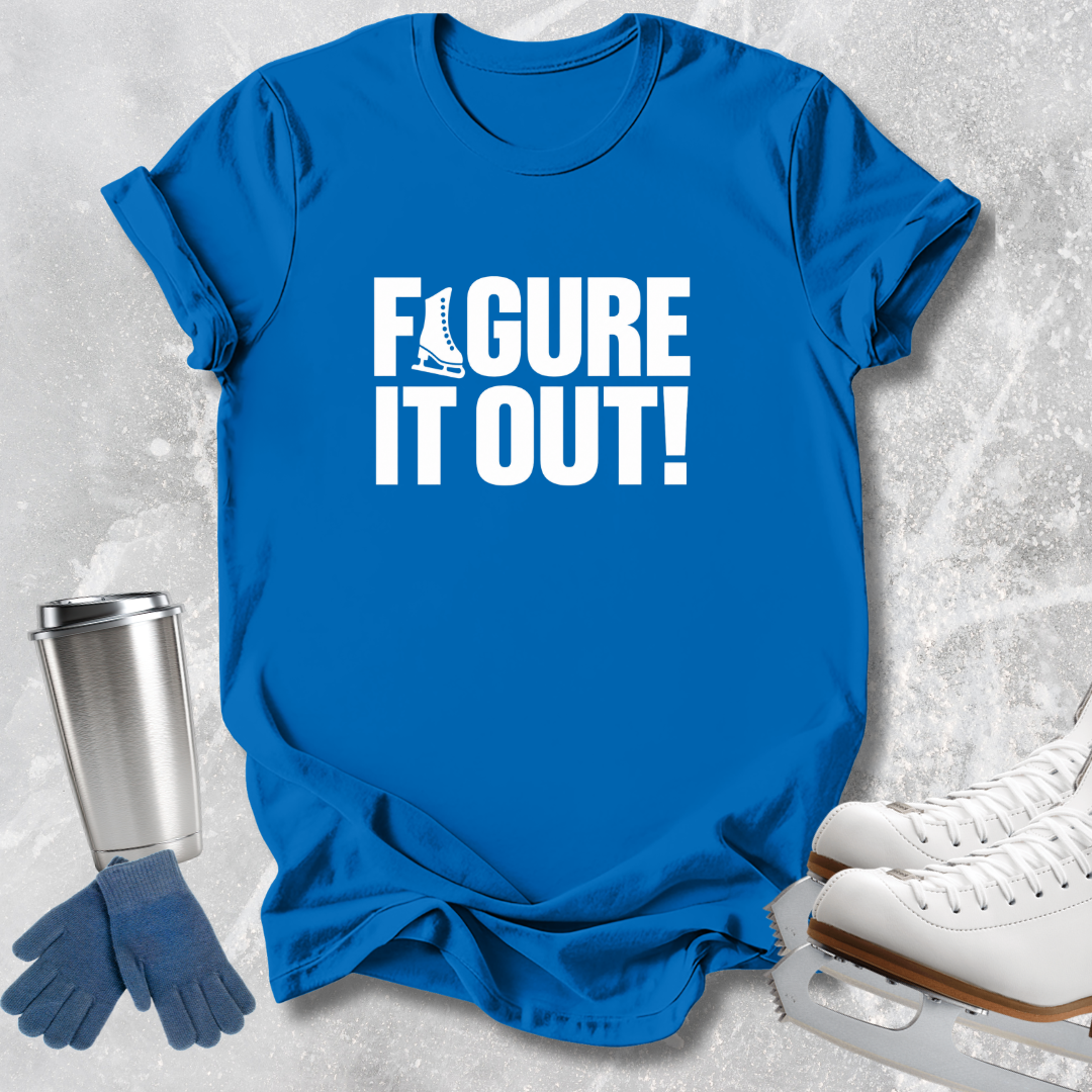 A bright blue short-sleeve T-shirt laid flat on a light gray textured surface, printed with the phrase 'FIGURE IT OUT!' in bold white letters. Ice skating props, including white ice skates, blue gloves, and a stainless steel travel mug, are arranged around the shirt.