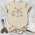 A beige graphic t-shirt featuring a black line art illustration of an ice skater with labeled parts, styled in a flat-lay with ice skates, gloves, and a travel tumbler on a textured gray background.
