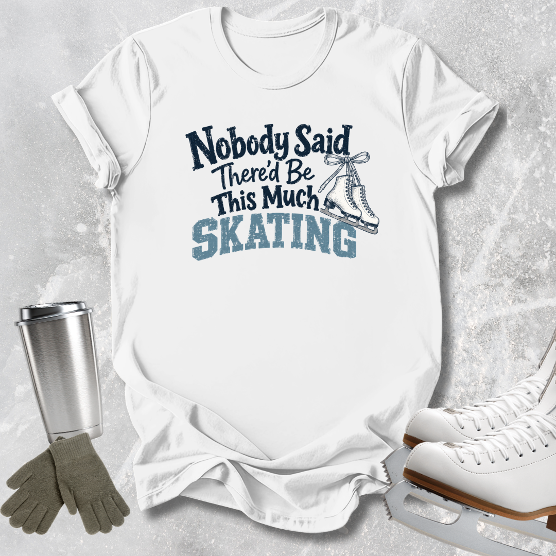 A white short-sleeve graphic T-shirt laid flat on a light gray textured surface, with the text 'Nobody Said There'd Be This Much SKATING' and a skater boot illustration. Ice skates, gloves, and a metal cup are arranged around the shirt as styled props.