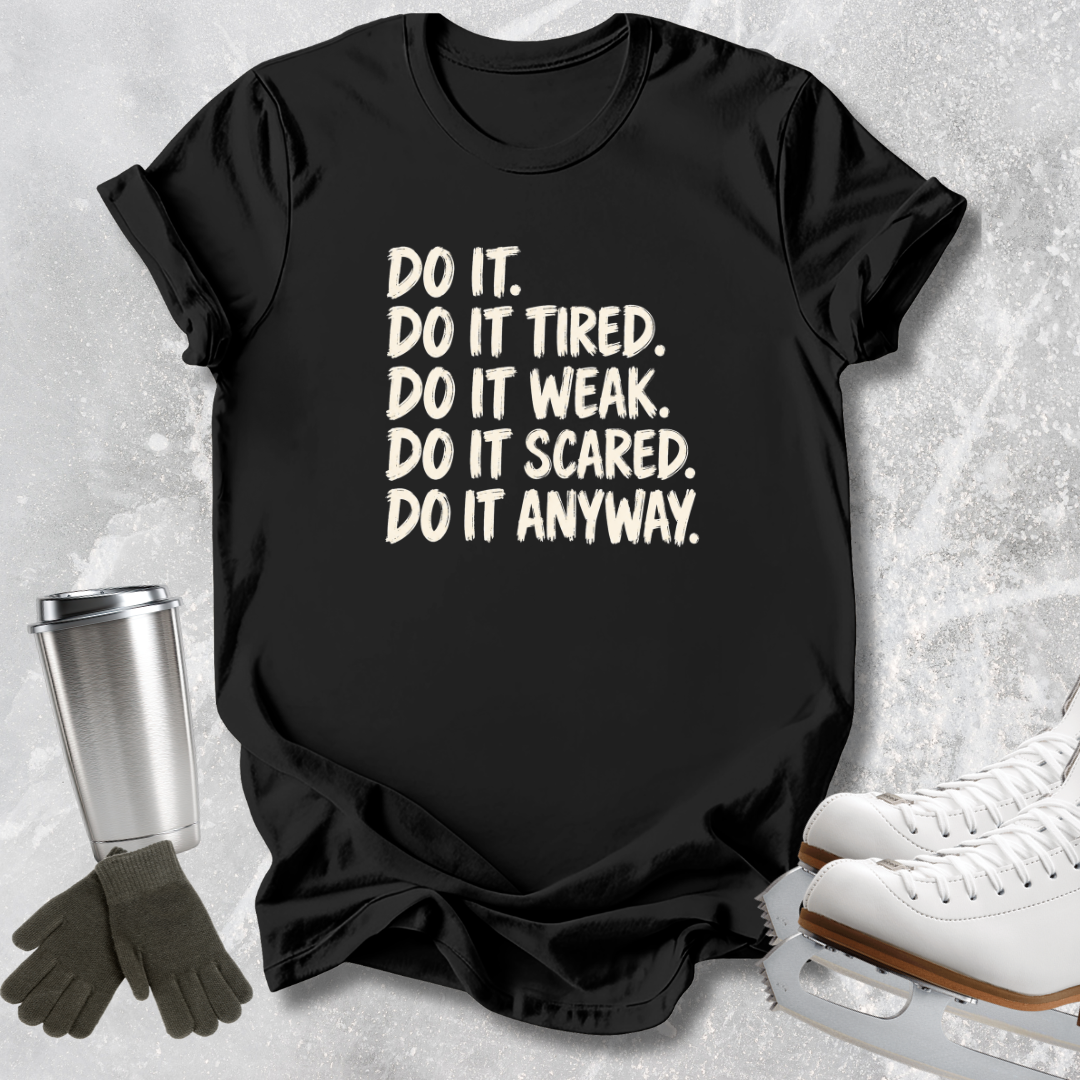 A black short-sleeve graphic T-shirt laid flat on a light textured surface, with cream text reading 'DO IT. DO IT TIRED.