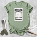 A sage green graphic t-shirt laid flat on a light gray textured background, styled with a stainless steel travel mug, gray gloves, and white ice skates. The t-shirt features a white ticket-style graphic that reads 'FIGURE SKATING DAUGHTER' with a list of expenses.