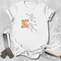 A white graphic t-shirt laid flat on a textured gray background, featuring a brown line drawing of two skaters and the words 'SKATE. FALL.