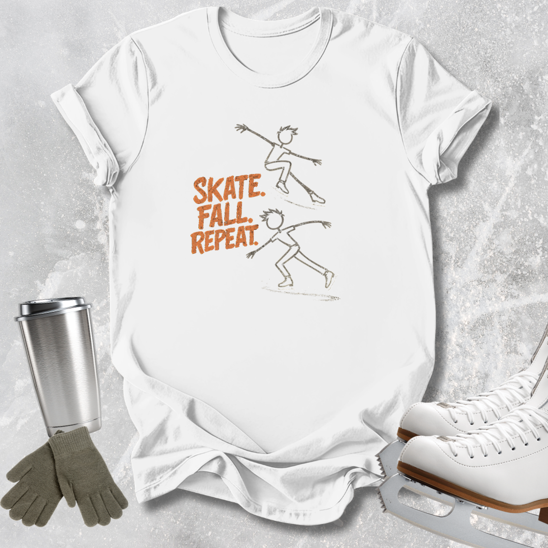 A white graphic t-shirt laid flat on a textured gray background, featuring a brown line drawing of two skaters and the words 'SKATE. FALL.