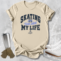 A beige graphic t-shirt laid flat on a light gray textured background, surrounded by ice skating props including white ice skates, a silver travel tumbler, and tan gloves. The t-shirt features the text 'SKATING IS TOOK OVER MY LIFE' in navy and blue lettering with a small skater graphic below.