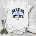 A white graphic t-shirt featuring the text 'SKATING IS TOOK OVER MY LIFE' in navy and blue lettering, styled in a flat-lay arrangement with ice skates, gloves, and a metal tumbler on a textured gray background.