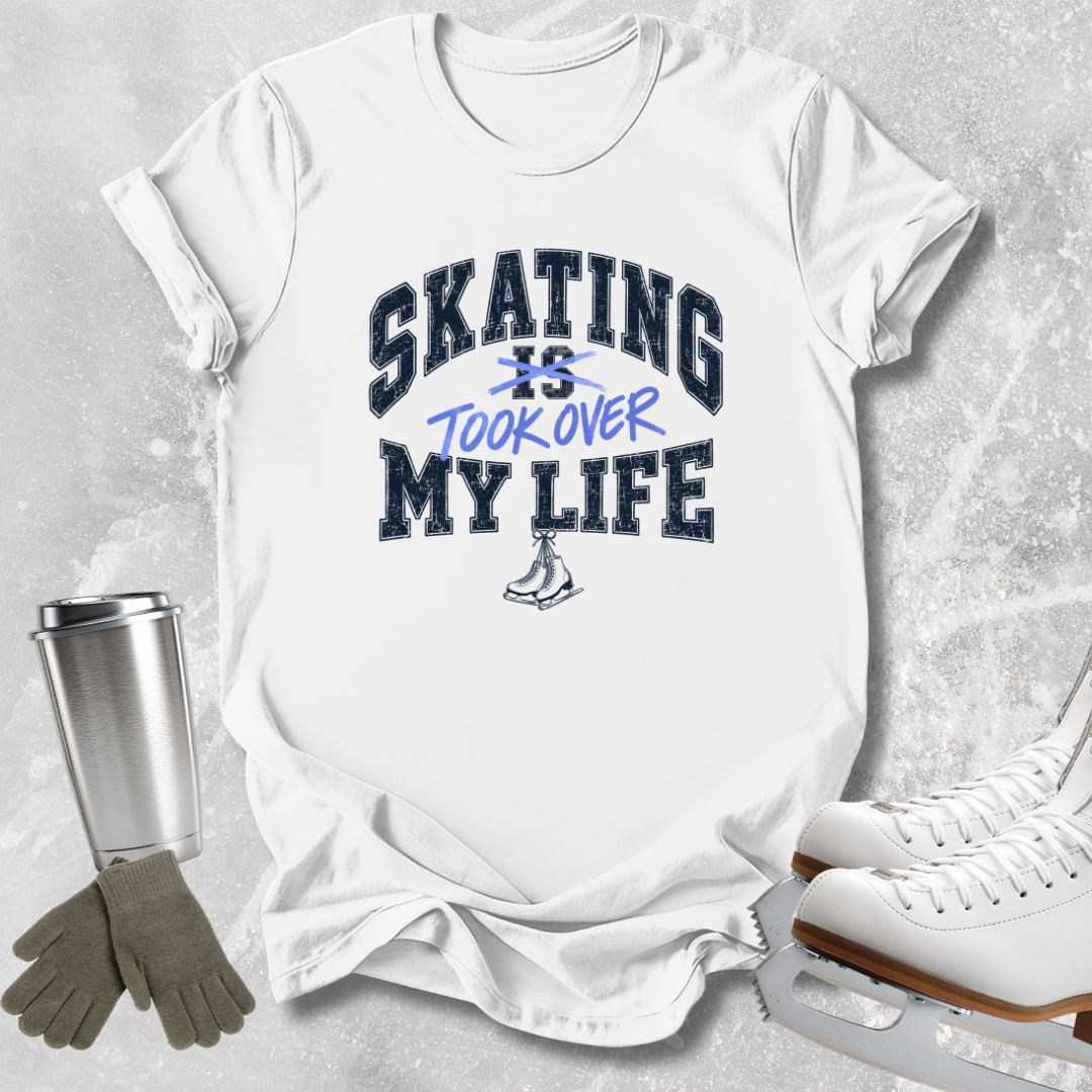 A white graphic t-shirt featuring the text 'SKATING IS TOOK OVER MY LIFE' in navy and blue lettering, styled in a flat-lay arrangement with ice skates, gloves, and a metal tumbler on a textured gray background.