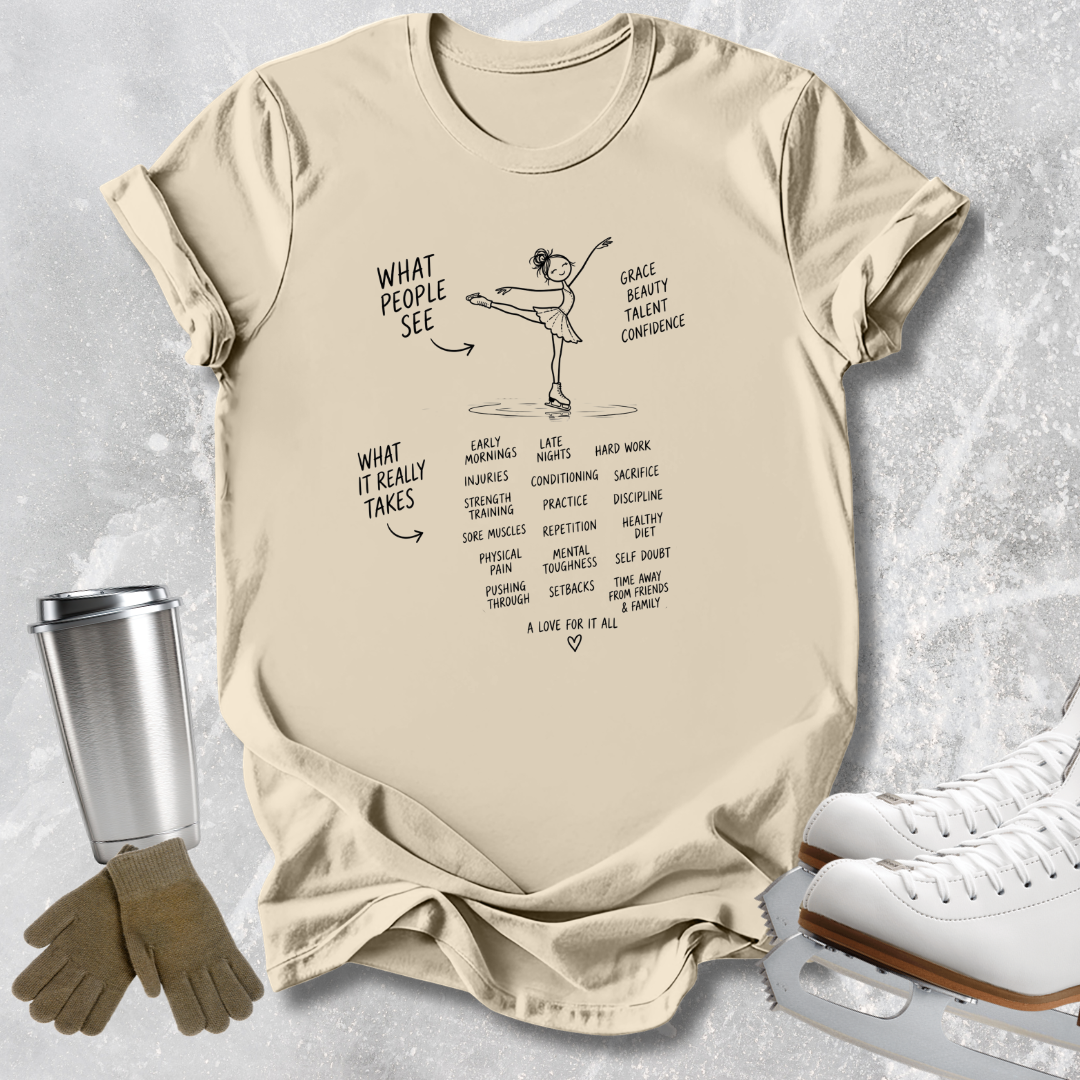 A beige graphic t-shirt featuring a black line art illustration of an ice dancer with text, styled in a flat-lay with ice skates, gloves, and a travel mug on a textured gray background.