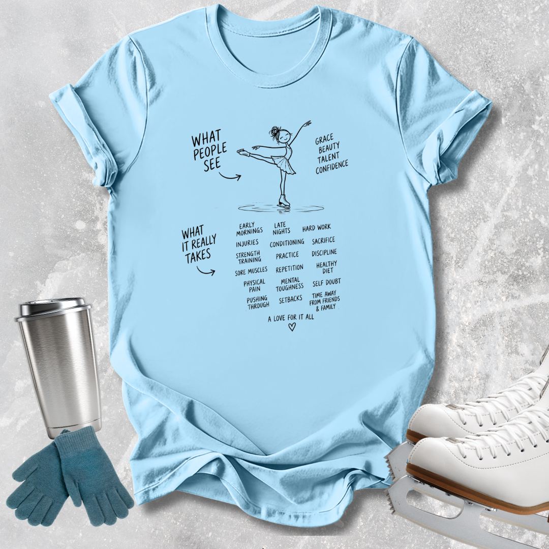 A light blue graphic t-shirt laid flat on a textured gray background, styled with ice skates, gloves, and a metal tumbler. The t-shirt features a black line drawing of a figure skater and text listing qualities like grace, toughness, confidence, and what it really takes.