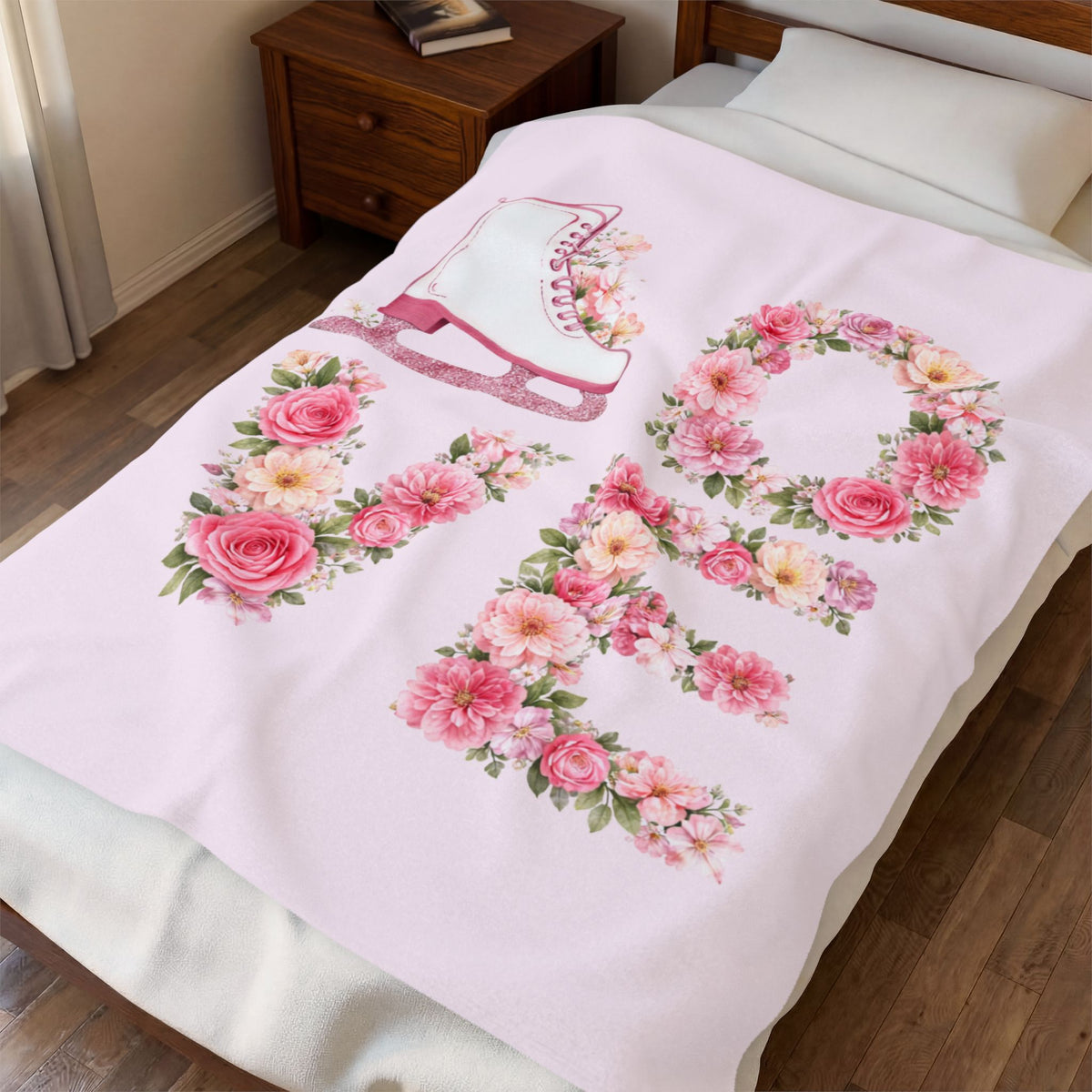 A light pink blanket with a large floral 'RO' design and a white ice skate motif, shown draped over a bed in a bedroom setting.